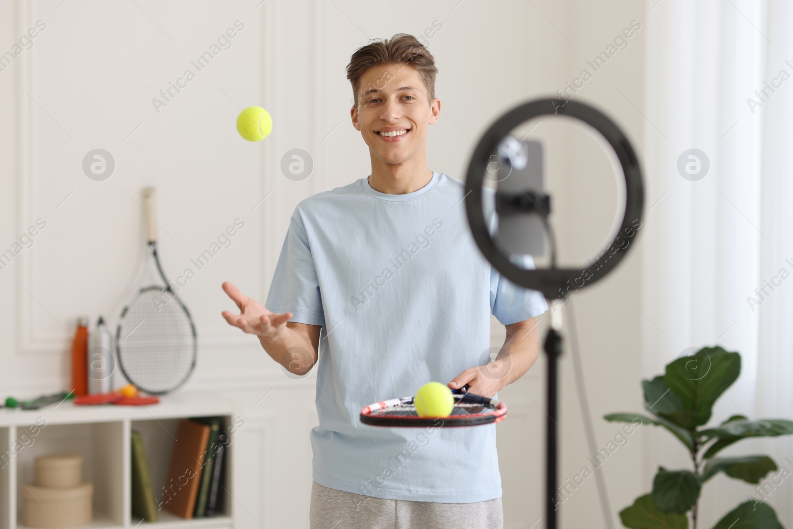 Photo of Smiling sports blogger with tennis racket and balls streaming online fitness lesson at home