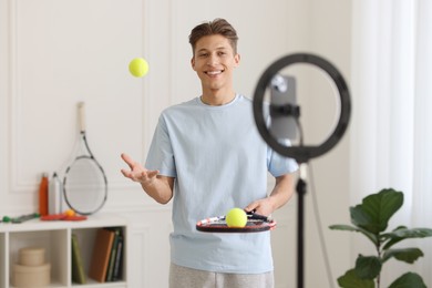 Smiling sports blogger with tennis racket and balls streaming online fitness lesson at home