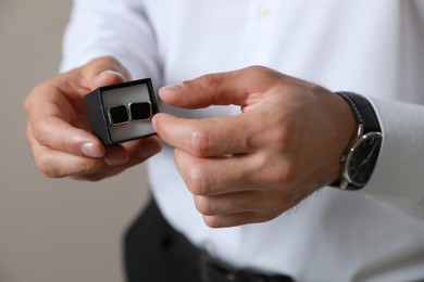 Photo of Stylish man holding box with cufflinks against beige background, closeup