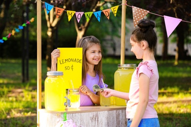 Cute little girl selling natural lemonade to kid in park. Summer refreshing drink