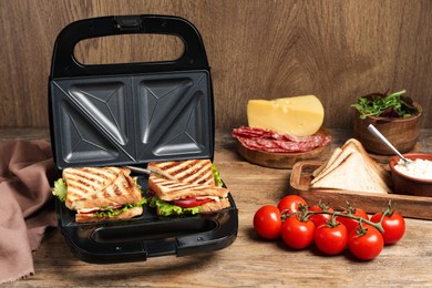 Photo of Modern grill maker with sandwiches and different products on wooden table