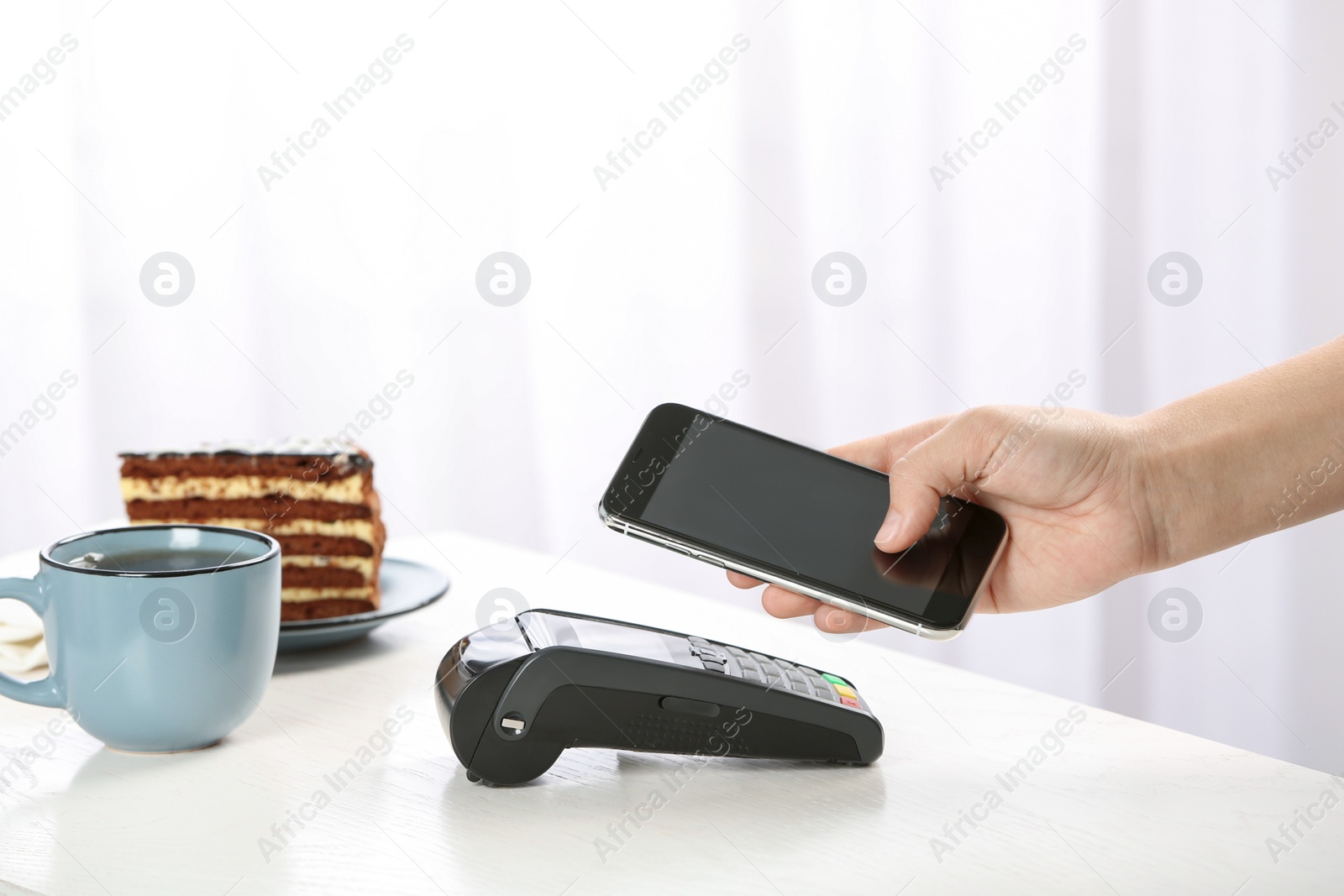 Photo of Woman using terminal for contactless payment with smartphone in cafe