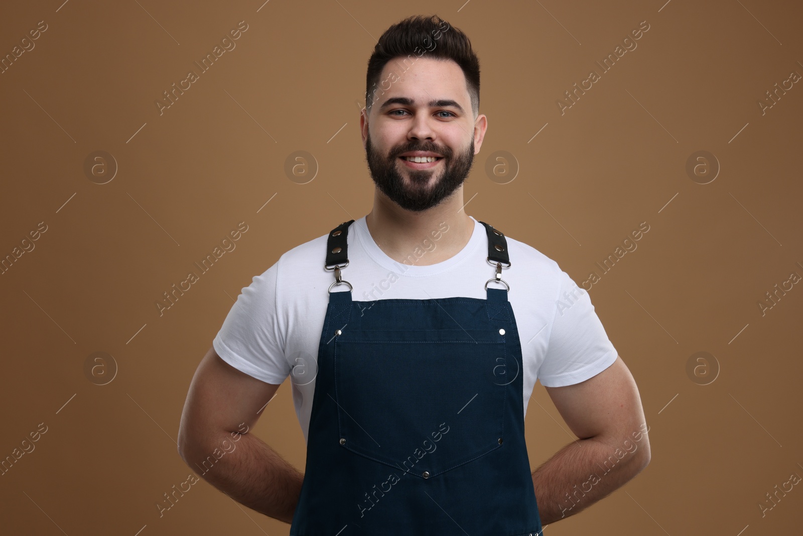 Photo of Smiling man in kitchen apron on brown background. Mockup for design