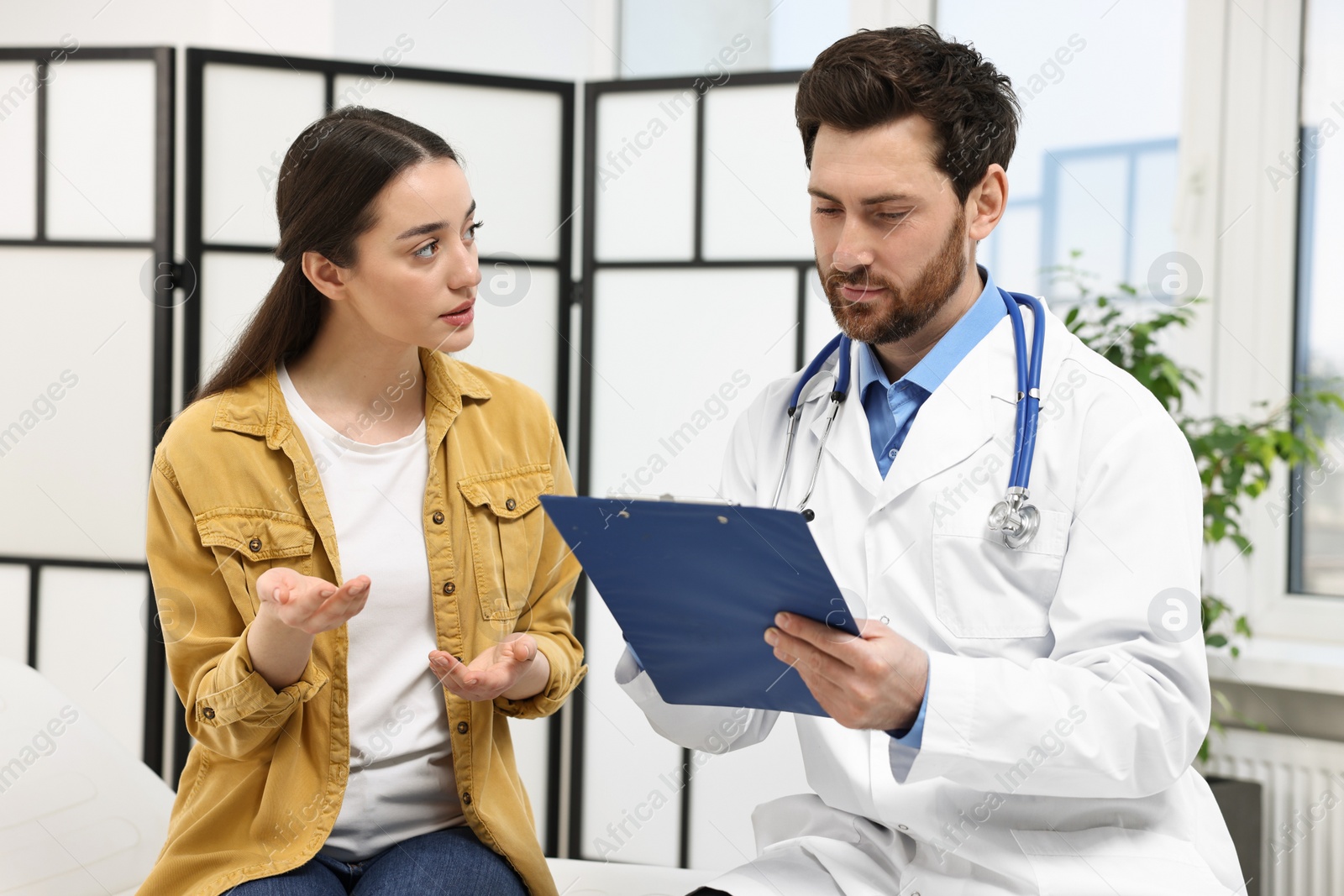 Photo of Doctor with clipboard consulting patient during appointment in clinic