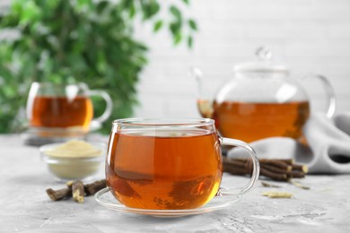 Aromatic licorice tea and dried sticks of licorice root on light gray textured table