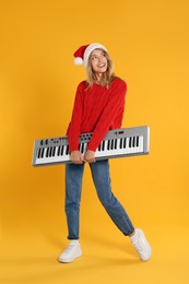 Young woman in Santa hat with synthesizer on yellow background. Christmas music
