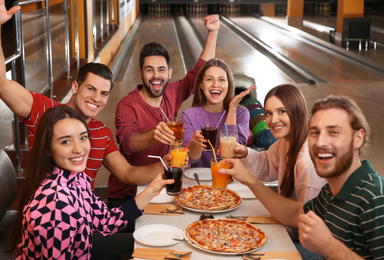Group of friends with drinks and pizza in bowling club