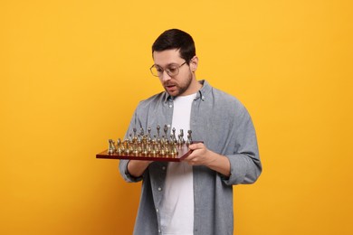 Emotional man holding chessboard with game pieces on orange background
