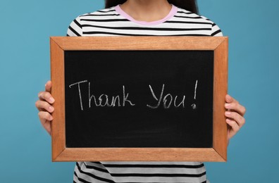 Photo of Woman holding small chalkboard with phrase Thank You on light blue background, closeup