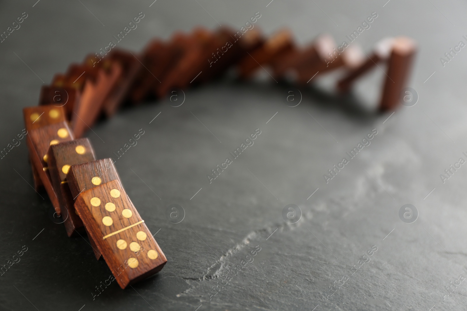 Photo of Wooden domino tiles falling on dark grey table. Space for text