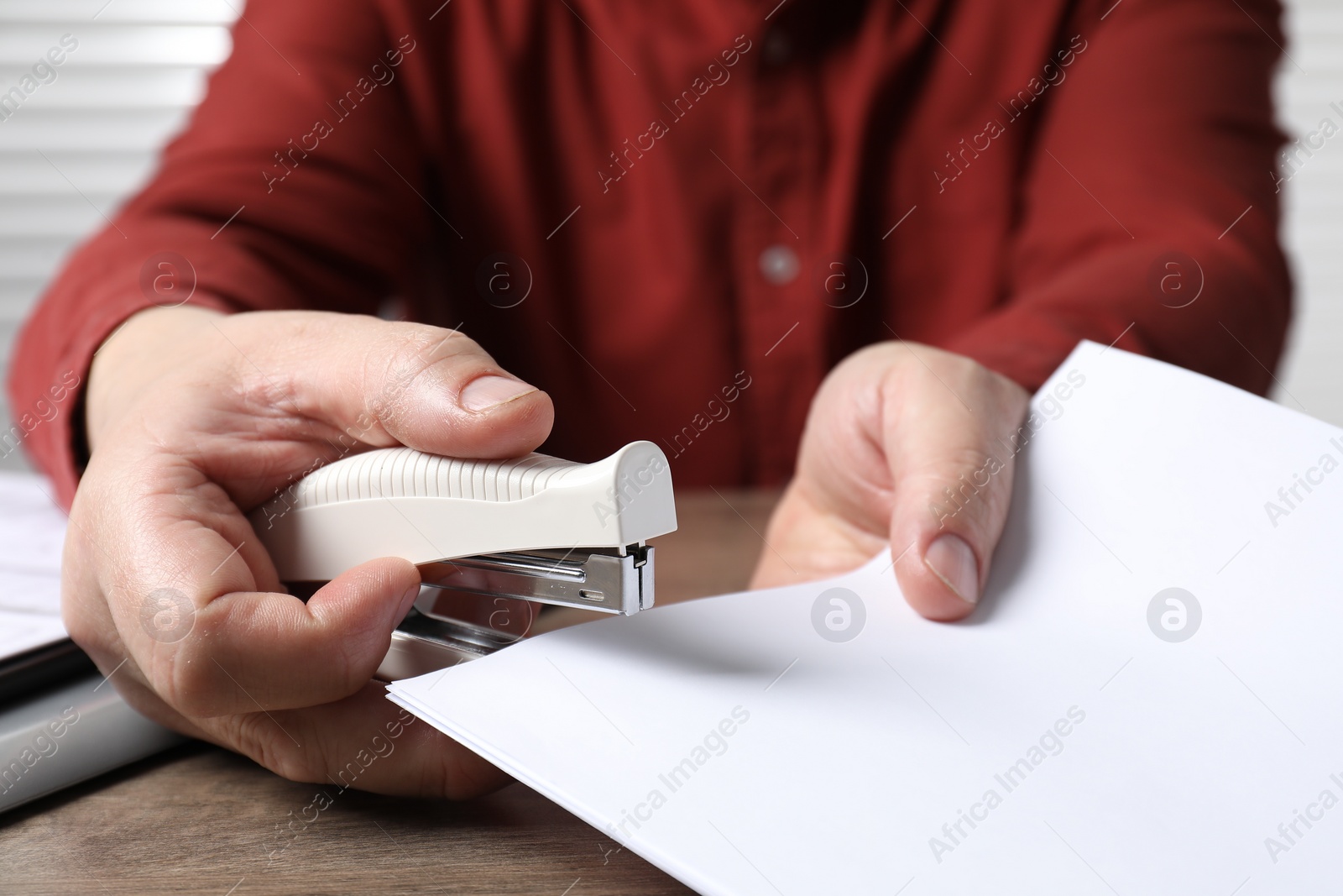 Photo of Man stapling papers at wooden table, closeup