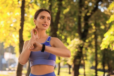 Attractive woman checking pulse after training in park on sunny day. Space for text