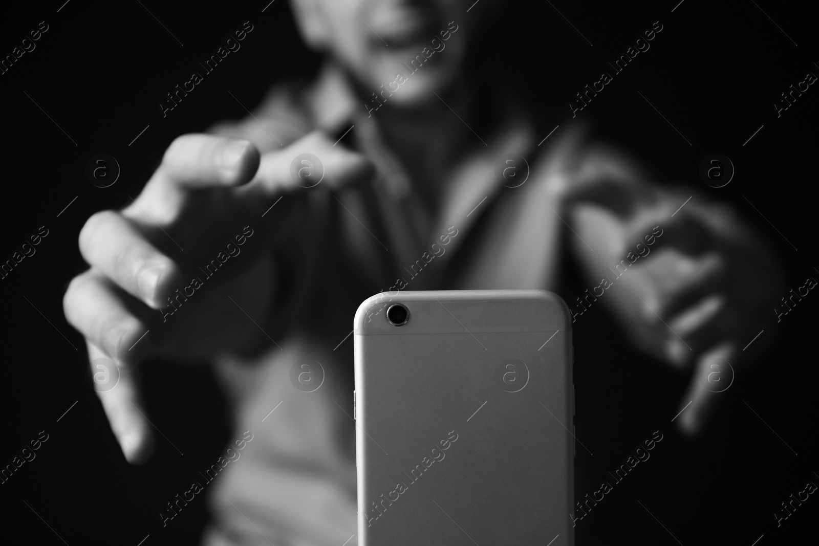 Photo of Emotional man reaching for smartphone on dark background, black and white effect. Addiction concept
