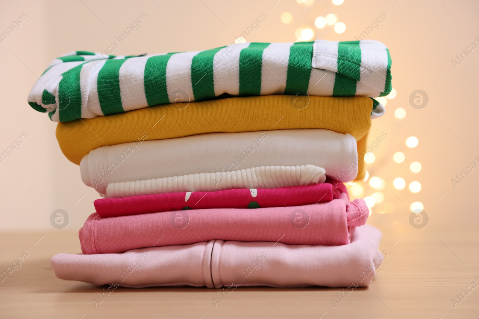 Stack of folded clothes on wooden table against beige background with blurred lights Photo of Stack of folded clothes on wooden table against beige background with blurred lights