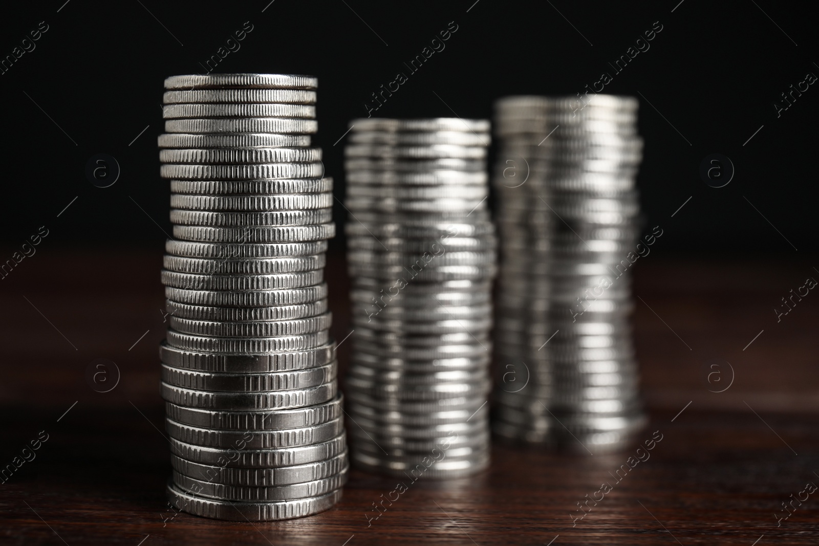 Photo of Many coins stacked on wooden table against black background