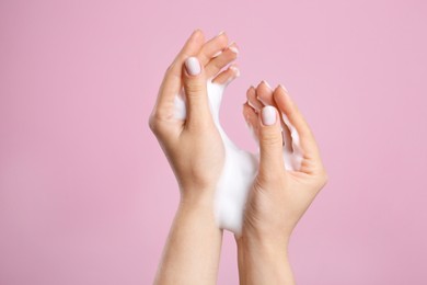 Photo of Woman washing hands with cleansing foam on pink background, closeup. Skin care cosmetic