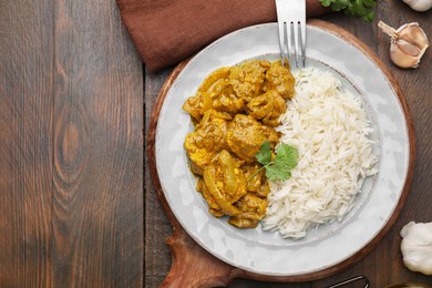 Photo of Delicious chicken curry with rice on wooden table, top view. Space for text