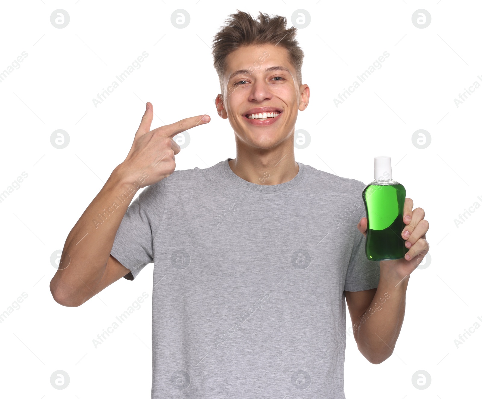 Photo of Young man with mouthwash pointing at his healthy teeth on white background