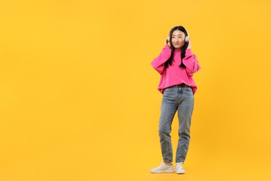 Photo of Portrait of beautiful woman in headphones on orange background. Space for text