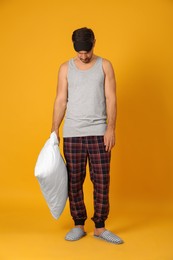 Photo of Man with pillow and eye mask in sleepwalking state on yellow background