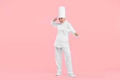 Photo of Happy professional confectioner in uniform holding whisk and spatula on pink background
