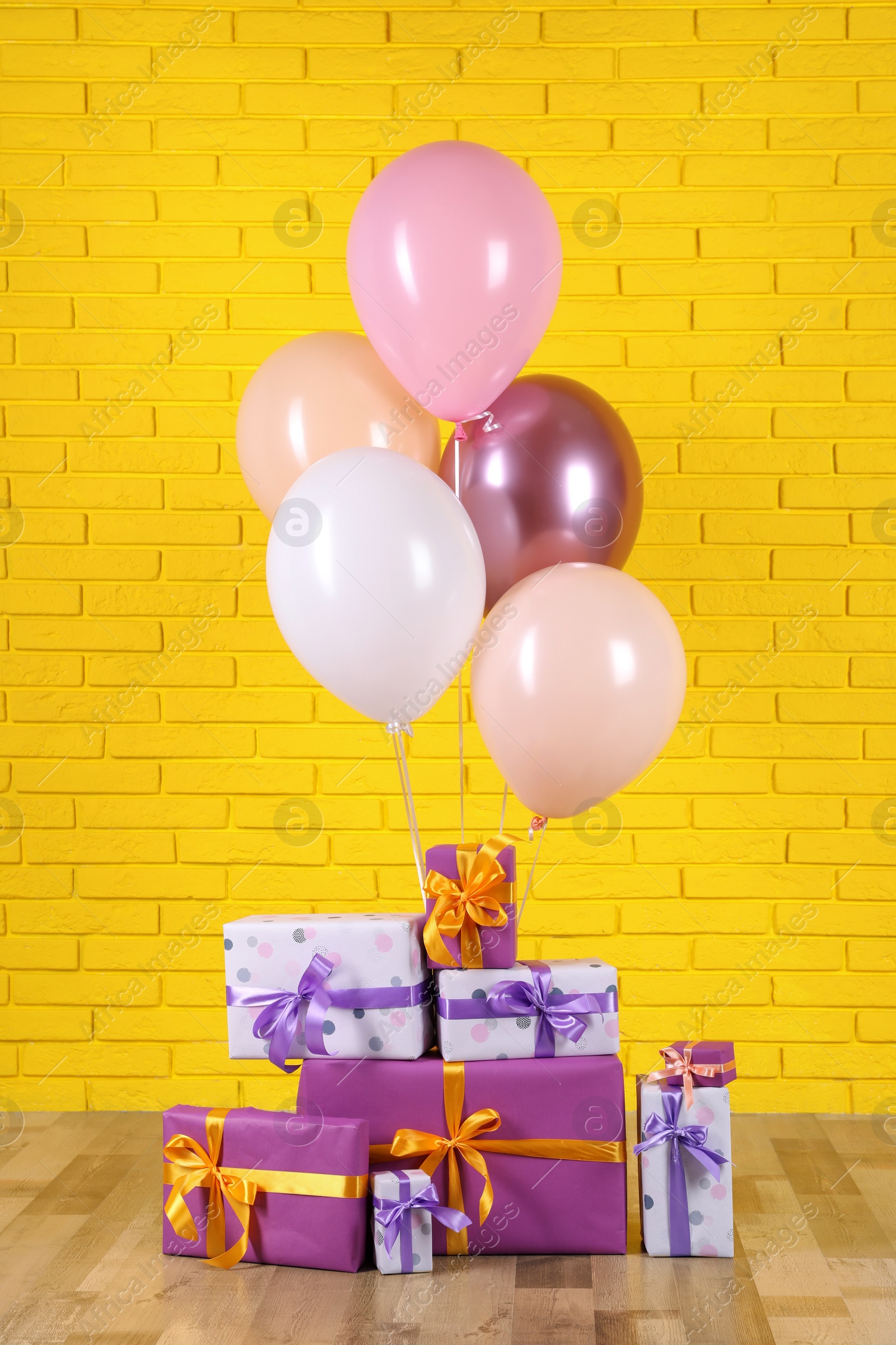 Photo of Many gift boxes and balloons near yellow brick wall