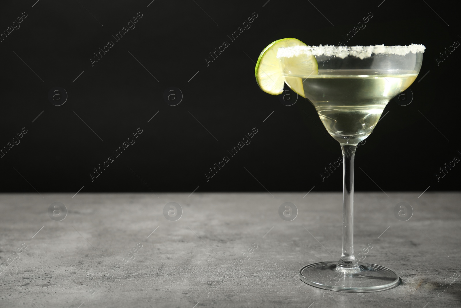 Photo of Glass of lemon drop martini cocktail with lime slice on grey table against black background. Space for text