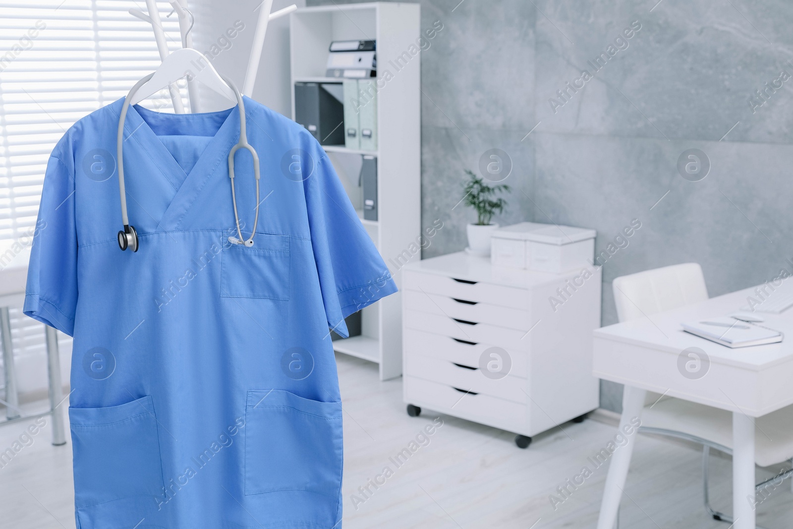 Photo of Blue medical uniform and stethoscope hanging on rack in clinic. Space for text