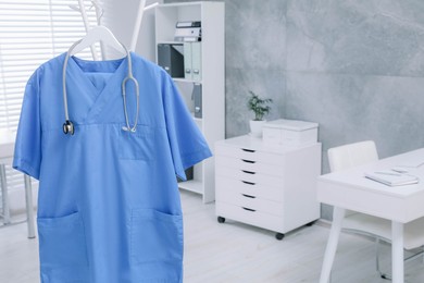 Photo of Blue medical uniform and stethoscope hanging on rack in clinic. Space for text
