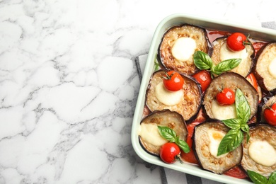 Photo of Baked eggplant with tomatoes, cheese and basil in dishware on marble table, top view. Space for text