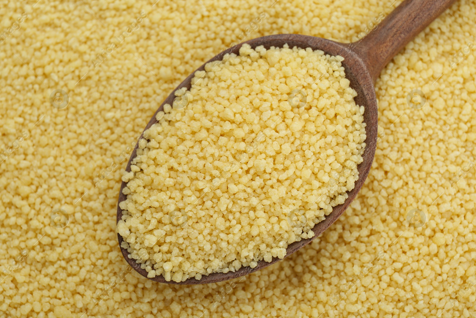 Photo of Spoon with raw couscous as background, top view
