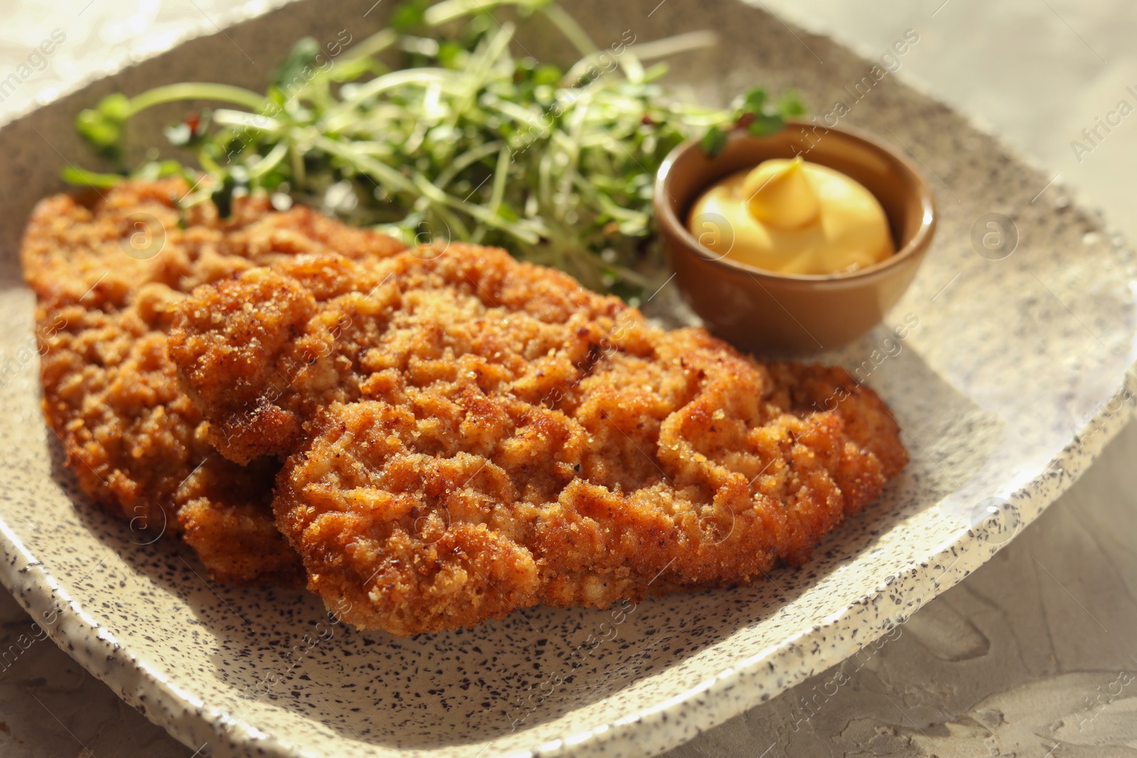 Photo of Tasty schnitzels served with sauce and microgreens on grey textured table, closeup