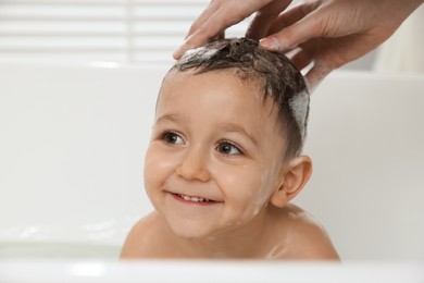 Photo of Mother washing her little son's hair with shampoo in bathroom