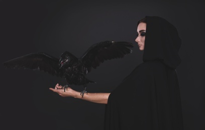 Mysterious witch with raven on black background