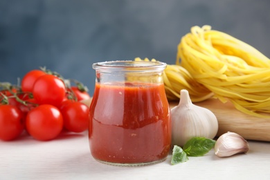 Photo of Jar of tasty tomato sauce with basil and garlic served on table