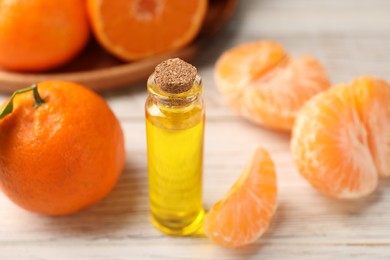 Bottle of tangerine essential oil and fresh fruits on white wooden table, closeup