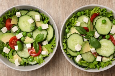 Photo of Tasty fresh salad with cucumber in bowls on wooden table, flat lay