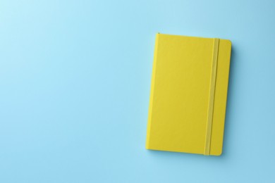 Photo of Closed yellow notebook on light blue background, top view. Space for text