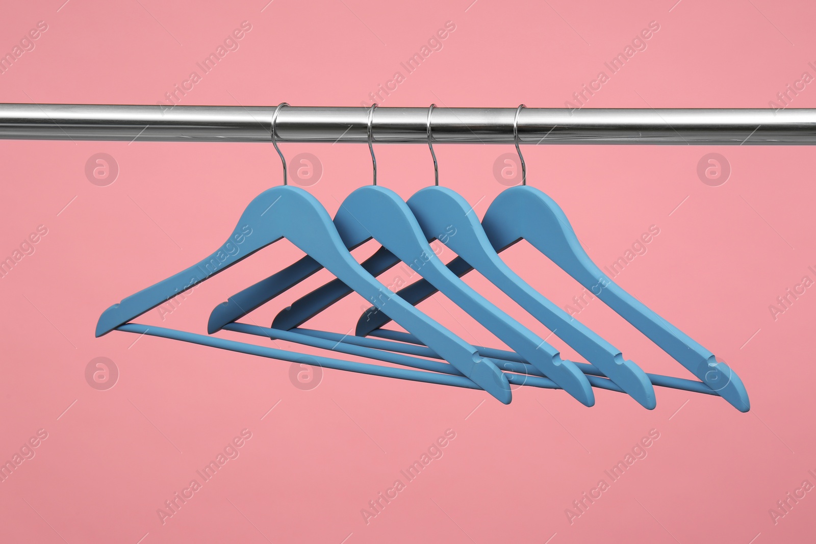 Photo of Empty clothes hangers on metal rail against color background