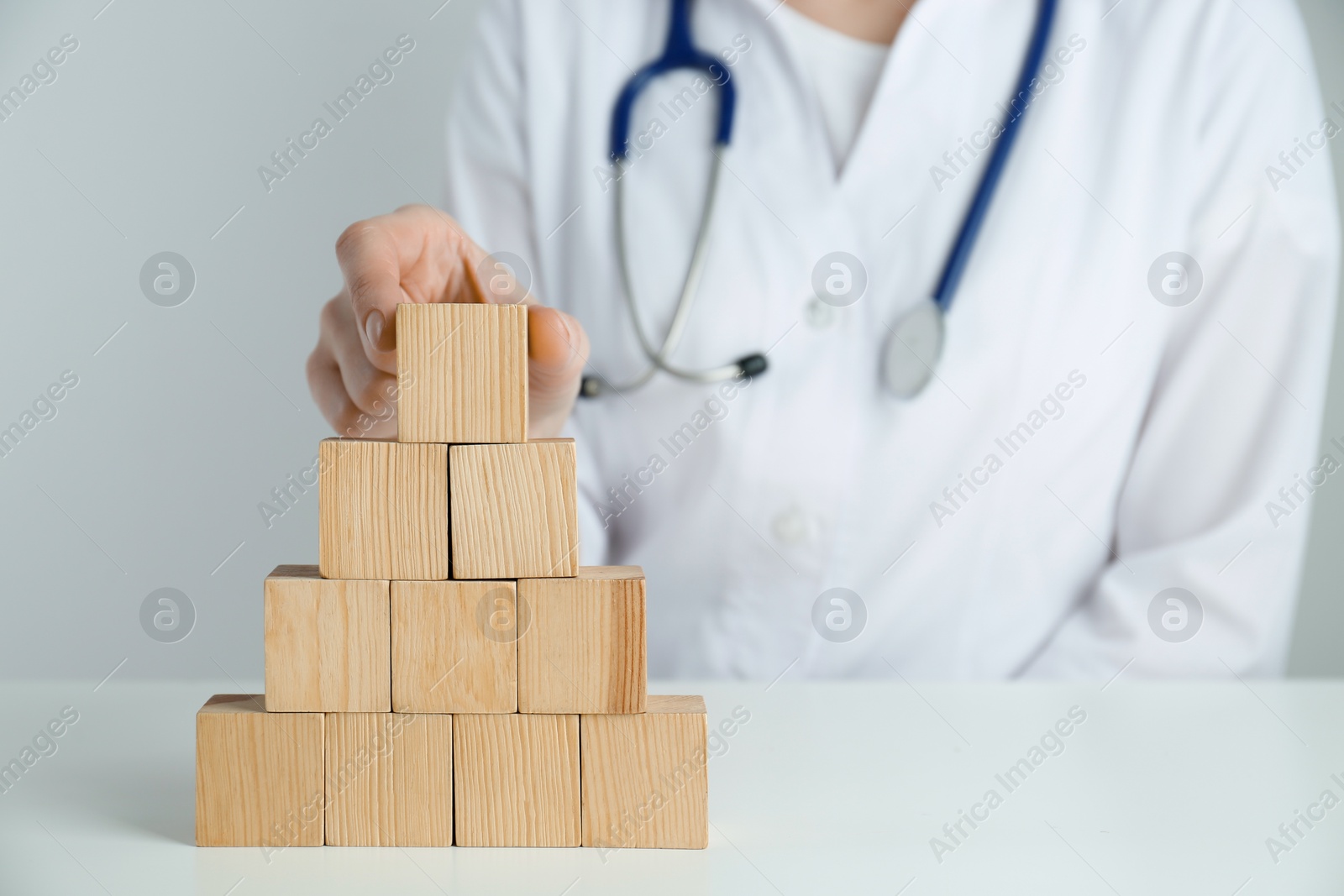 Photo of Doctor building pyramid of blank wooden cubes on white table against light background, closeup. Space for text