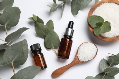 Aromatherapy products. Bottles of essential oil, sea salt and eucalyptus leaves on white background, flat lay