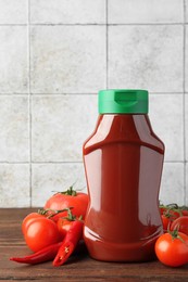 Photo of Bottle of tasty ketchup, tomatoes and chili pepper on wooden table