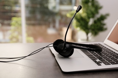 Photo of Modern laptop and headset on table indoors. Technical support concept