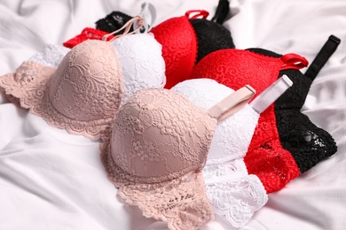 Photo of Beautiful lace bras on white bed sheet. Stylish underwear