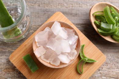 Aloe vera gel and slices of plant on wooden table, flat lay