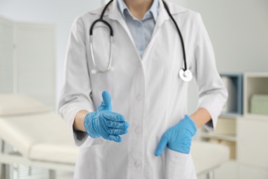 Female doctor in gloves offering handshake indoors, closeup