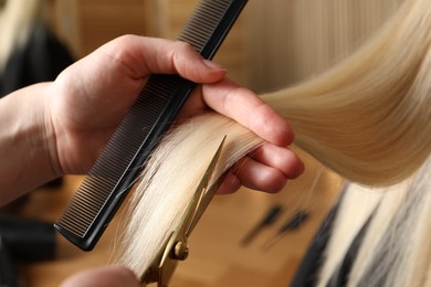 Photo of Hairdresser cutting client's hair with scissors in salon, closeup