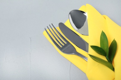 Photo of Folded napkin with fork, spoon and knife on grey background, closeup