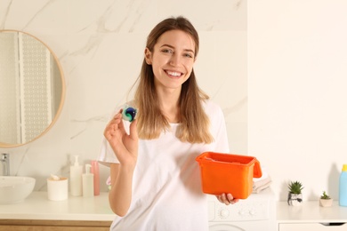 Woman holding container with laundry detergent capsules in bathroom