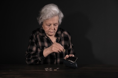 Poor mature woman putting coins into wallet at table. Space for text